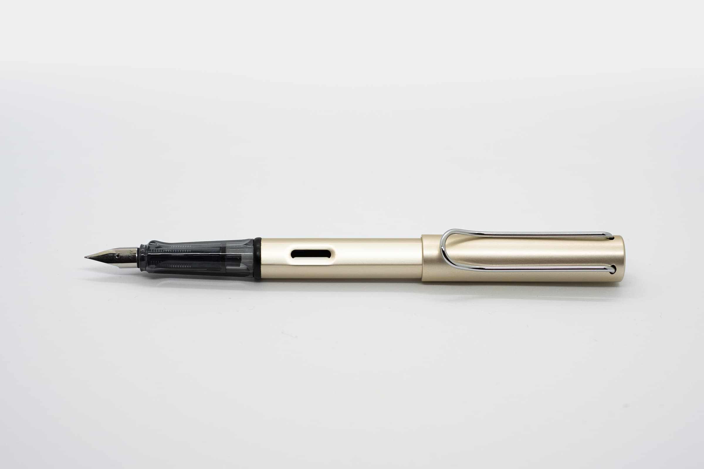 白い背景に横向きに置いたLAMY AL-star シャンパンゴールド。淡いシャンパンゴールドの軸とキャップ、透明スモークのグリップとシルバーのニブ、クリップ