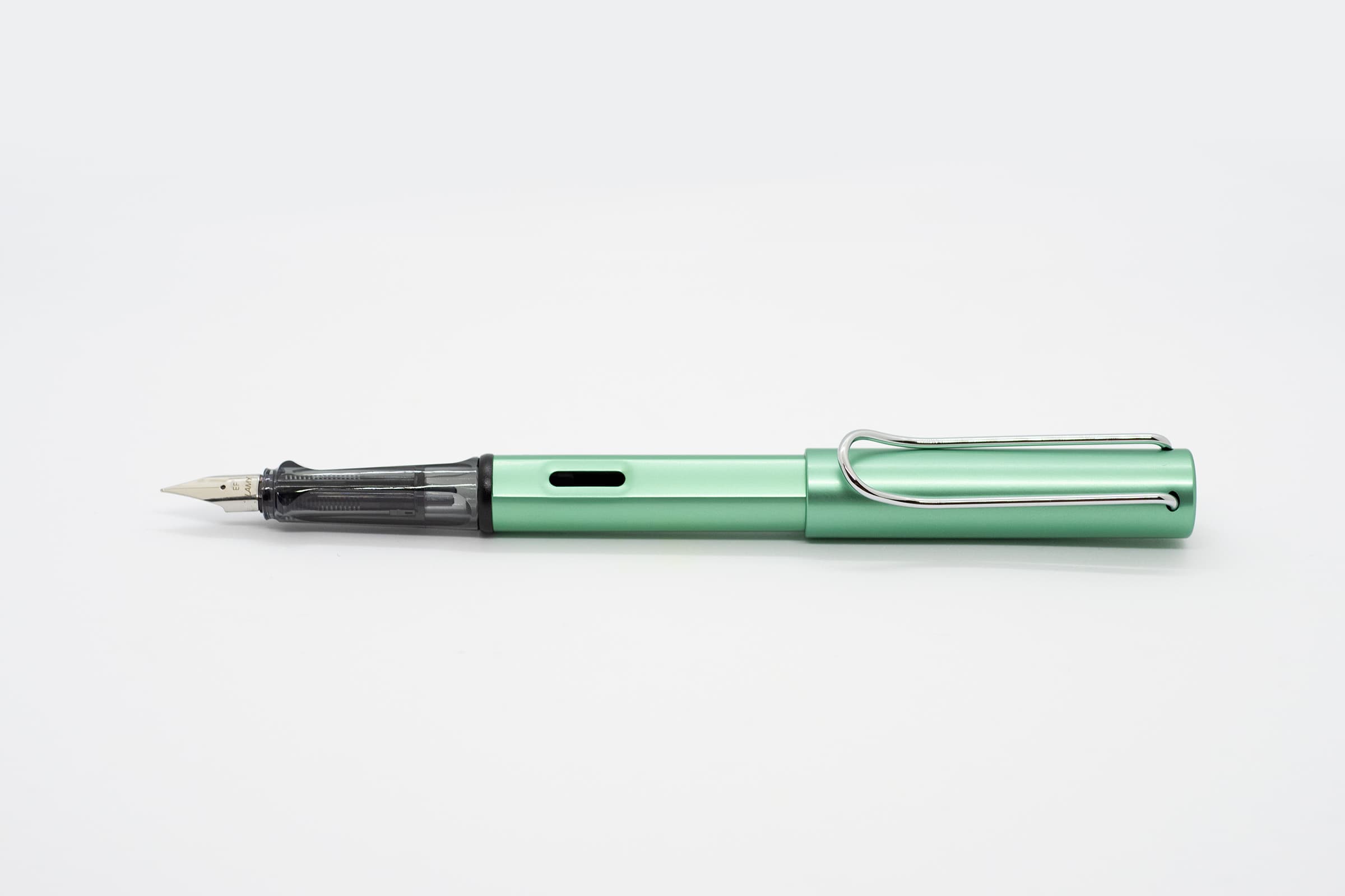 白い背景に横向きに置いたLAMY AL-star ブルーグリーン。淡いブルーグリーンの軸とキャップ、透明スモークのグリップとシルバーのニブ、クリップ