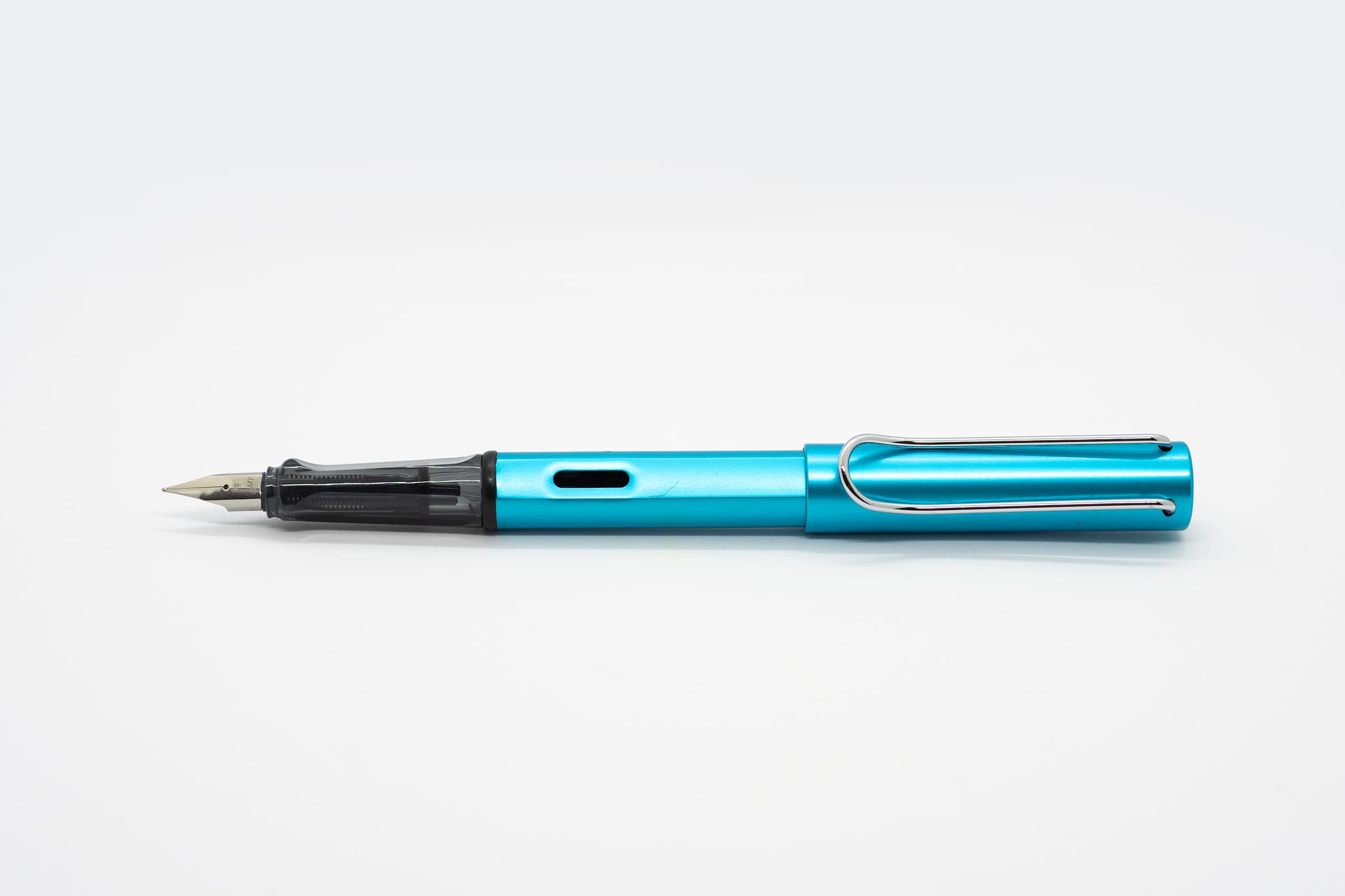白い背景に横向きに置いたLAMY AL-star パシフィック。鮮やかなターコイズブルーの軸とキャップ、透明スモークのグリップとシルバーのニブ、クリップ