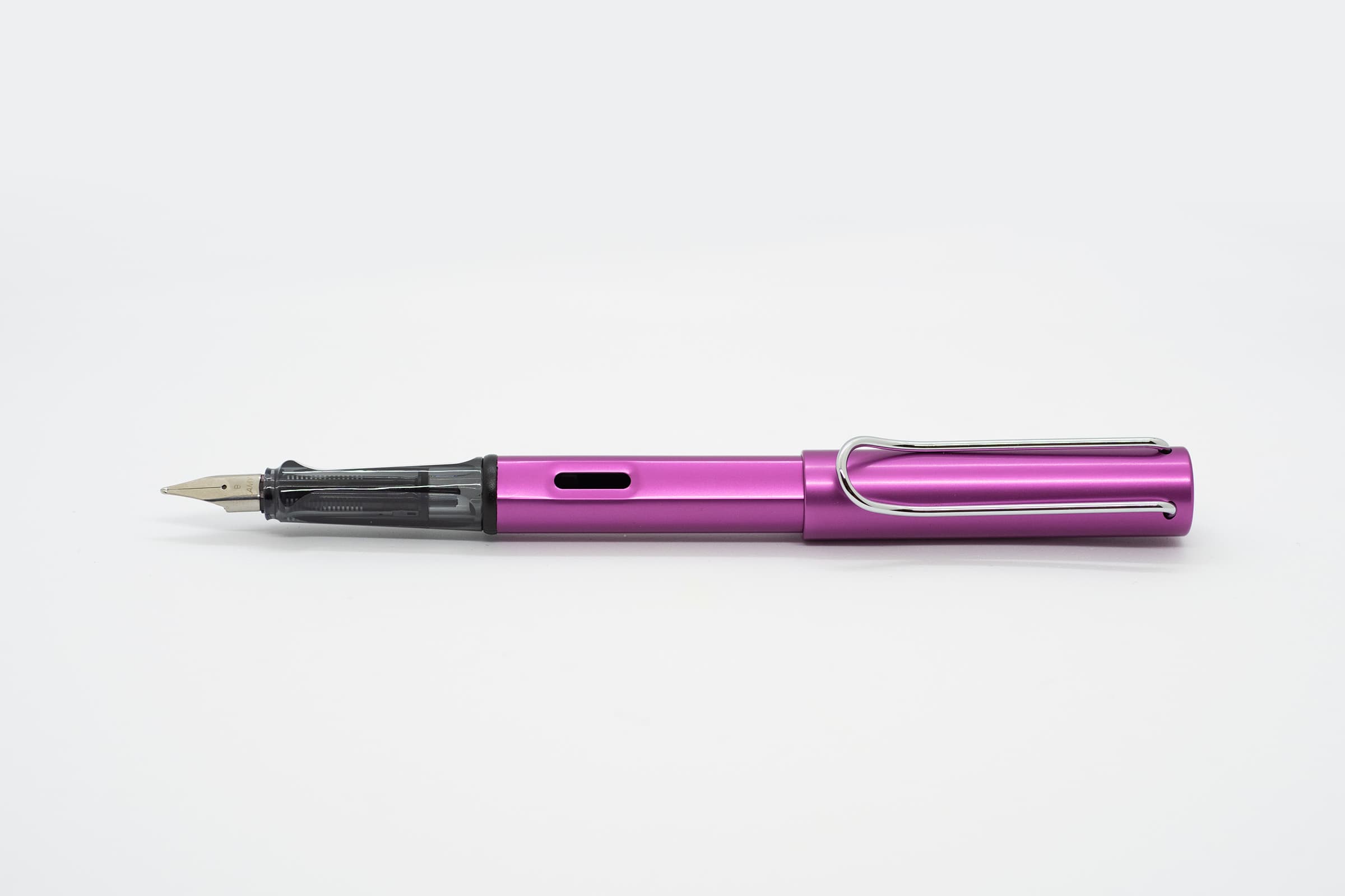 白い背景に横向きに置いたLAMY AL-star ヴァイブラントピンク。鮮やかな紫みのピンクの軸とキャップ、透明スモークのグリップとシルバーのニブ、クリップ