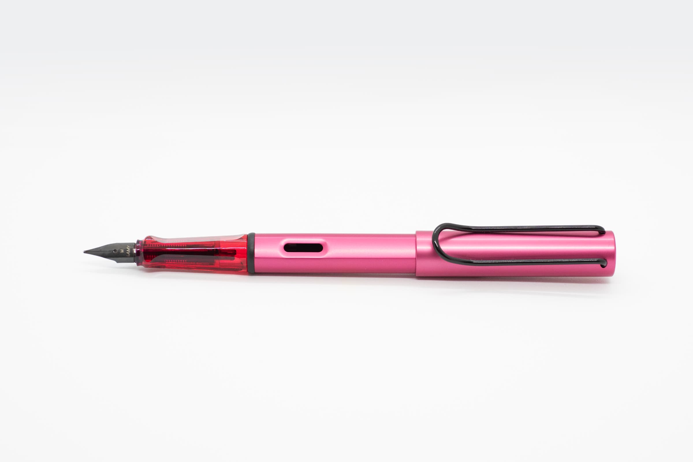 白い背景に横向きに置いたLAMY AL-star ファイアリー。鮮やかなピンクの軸とキャップ、透明レッドのグリップと黒いニブ、クリップ